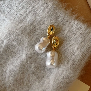 Detail of gold oval studs with baroque irregular pearls on gray knit background