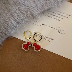 Detailed close-up of gold gourd earrings with red beads and sparkling white zircons