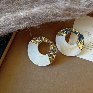Detail of acrylic and hammered metal geometric hoop earrings on brown leather