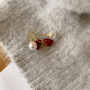 Elegant red heart earrings with white pearls and gold hooks on grey knit texture