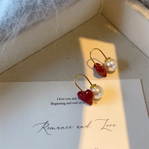 Elegant gold earrings featuring red enamel hearts and white pearls on a romantic card
