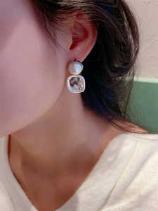 Détail d'une boucle d'oreille carrée en métal argenté avec perle blanche portée