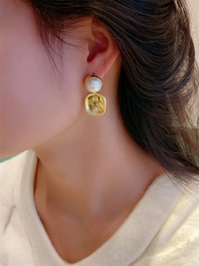Gros plan de boucles d'oreilles carrées dorées brossées avec perle blanche sur modèle