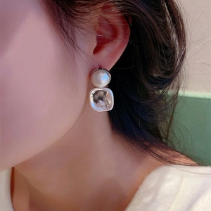 Boucles d'oreilles carrées en métal brossé avec perle blanche portées par un mannequin