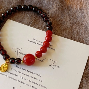 Garnet beaded bracelet with red stone and golden Fu character pendant on plush background