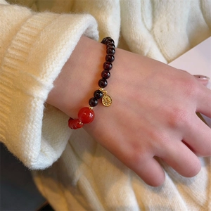 Garnet beaded bracelet with gold Fu pendant and red bead on a knit sweater background