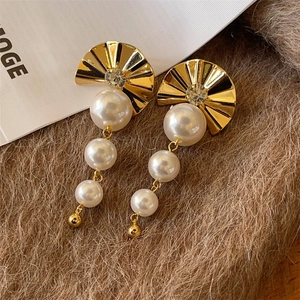 Elegant gold fan earrings with cascading white pearls on a soft brown plush background