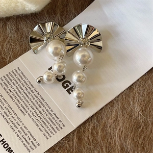 Macro view of silver fan-shaped earrings featuring pleat textures and tiered pearls