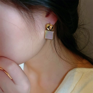 Boucles d'oreilles carrées en nacre avec clous dorés texturés portées à l'oreille