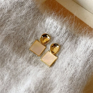 Vue détaillée de boucles d'oreilles dorées géométriques avec nacre carrée sur tissu gris