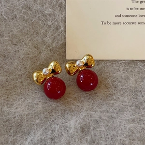 Red pearl bow stud earrings in gold metal on a grey plush background, luxury style