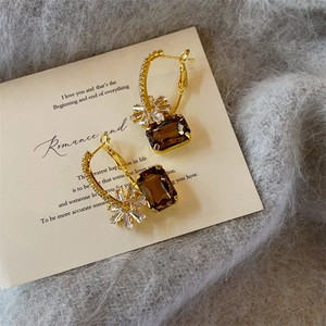Macro detail of gold flower earrings with coffee-colored square stones and zircon stones