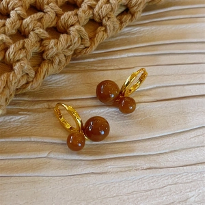 Detail of gold hoop earrings featuring asymmetrical brown tiger eye stone double beads