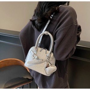 Close-up of silver metallic handbag featuring heart charm and chain on a female model