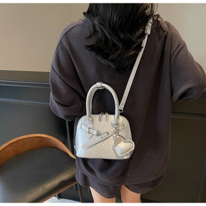 Detail of silver shell bag with heart charm and leather strap worn by a model
