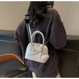 Rear view of a silver shell bag with a heart charm and textured finish on a model