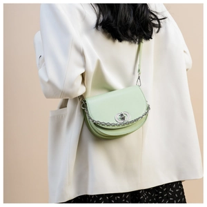 Detail of mint green half-moon saddle bag with silver chain worn by a model in casual blazer