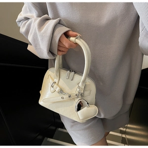 Detail view of cream shell bag featuring silver chain decor and heart-shaped pendant charm