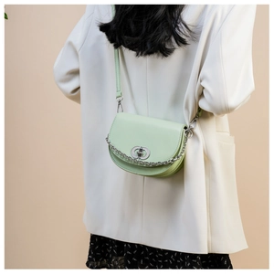Detail of mint green saddle bag featuring silver chain and circular buckle on a model