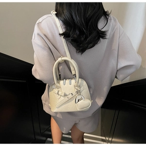 Back view of a model wearing a cream shell-shaped handbag with a heart charm and chain