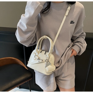 Creamy white shell bag detail with heart charm and crossbody strap shown on a model