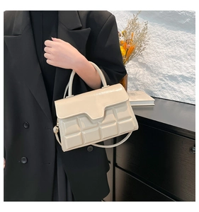 Detail der cremeweißen Handtasche mit geprägter Schokoladengitter-Struktur und glatter Klappe