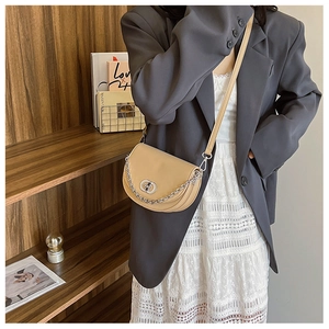Detail of beige saddle bag featuring silver chain decor and metal turn-lock on strap