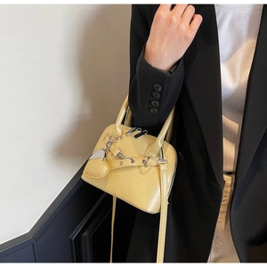 Detail of yellow shell handbag featuring metal chain and heart pendant with shoulder strap