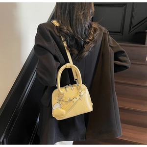 Detail of yellow shell handbag with heart charm carried by a model in black blazer