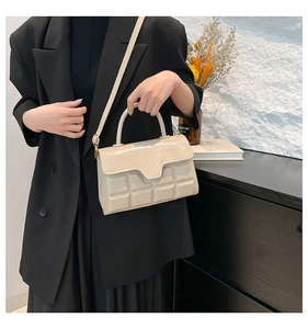 Detail der cremeweißen Handtasche mit Gitterprägung und glänzender Lackoberfläche