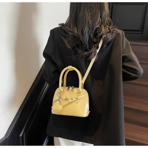 Detail of yellow shell handbag with heart charm worn by model over a black blazer