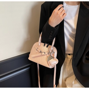 Detail view of light pink shell handbag featuring heart pendant and leather buckle strap