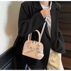 Pink shell handbag with heart pendant shown as a crossbody bag on a model in a warm setting