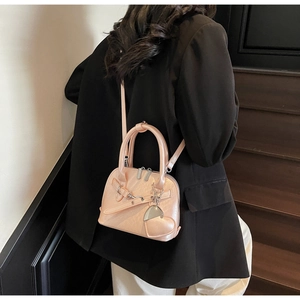 Detail of light pink shell-shaped bag with heart charm shown on a black suit
