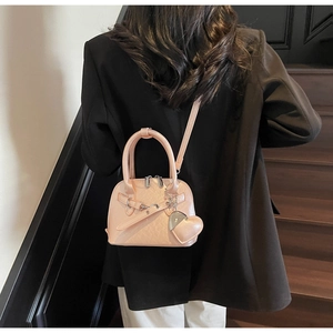 Mini shell-shaped handbag in light pink PU leather worn as a stylish crossbody bag