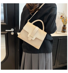 Detail of beige faux crocodile leather bag with gold hardware and top handle strap