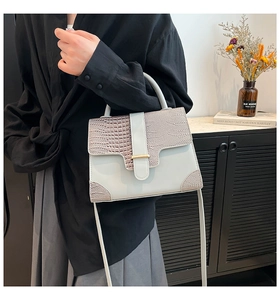 Detail of light gray faux leather handbag with crocodile pattern and golden metal buckle