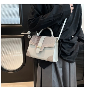 Detail of grey crossbody bag with crocodile pattern flap and golden metal clasp lock