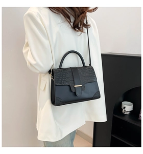 Detail of black faux crocodile leather handbag with metal buckle worn by a model
