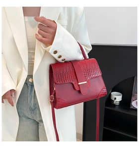 Detail of dark red crocodile embossed leather handbag with gold clasp on model