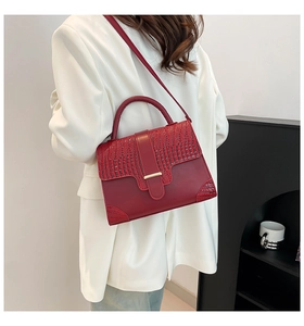 Detail of dark red crocodile pattern handbag with gold metal clasp on white suit