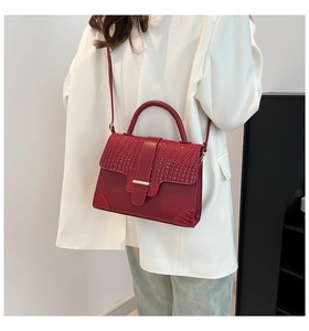 Detail of red crocodile texture handbag with gold metal clasp and slim shoulder strap