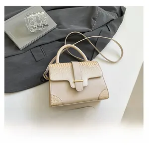 Detail of cream crossbody bag with faux crocodile texture and gold rectangular clasp
