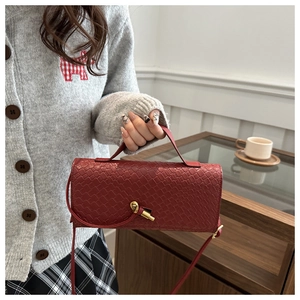 Détail du sac bandoulière tressé bordeaux avec boucle en métal doré porté par un mannequin