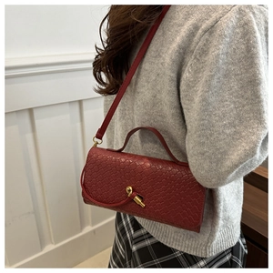 Détail du sac à main en cuir tressé rouge foncé avec fermoir doré porté à l'épaule