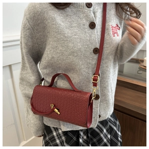 Détail de la texture en cuir tressé bordeaux et du fermoir en métal doré de ce sac chic