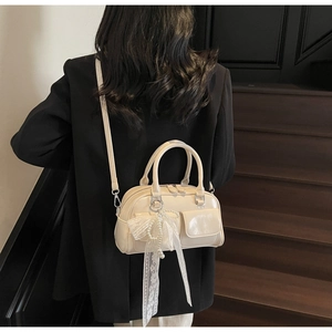 Detail of cream Boston bag with pearl and lace bow charm on a leather surface