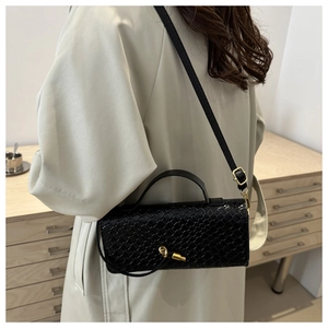 Détail du sac à bandoulière en cuir tressé noir avec fermoir doré sur un trench