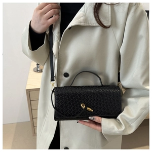 Détail du sac à main noir tressé avec fermoir nœud doré porté sur un trench beige