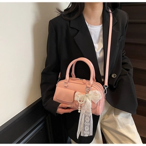 Detail of pink patent leather handbag with lace bow and pearl charm on shoulder